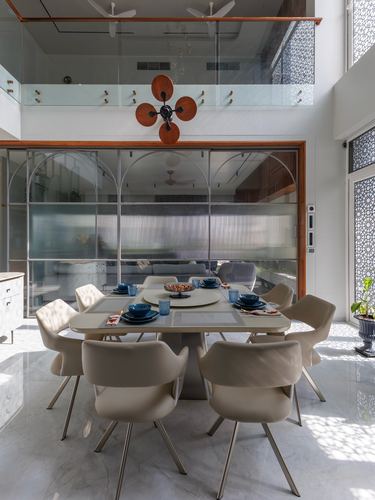 Double-height dining room with arched glass partitions, marble floor, cane chairs, and a decorative orange wall fan