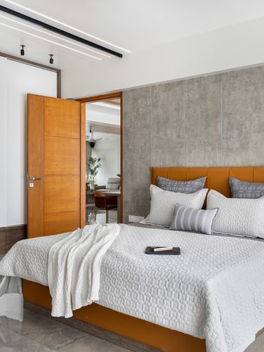 Bedroom with mustard leather headboard, grey textured wall panels, and open wooden door to living area