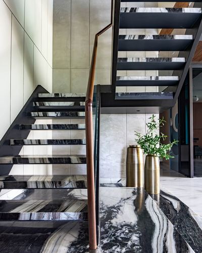 Marble-clad floating staircase with glass balustrade and brass vases in a Nagpur home