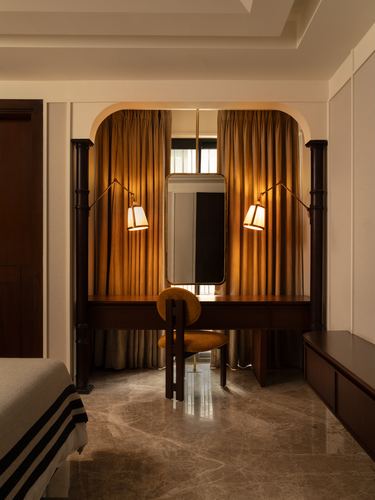 Arched alcove dressing nook with mirror, mustard curtains, brass sconces and marble floor