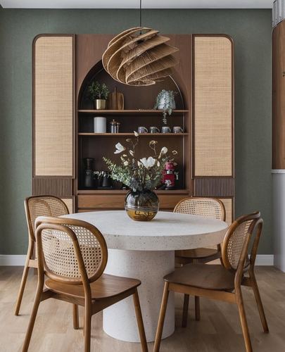 Round terrazzo dining table with cane chairs beneath a woven pendant light against a sage green wall