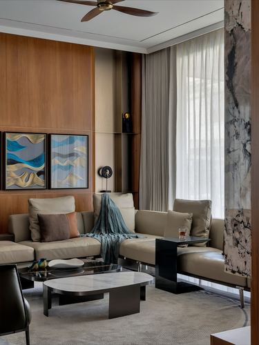 Living room with taupe sectional sofa, wood panelled wall, and veined stone column