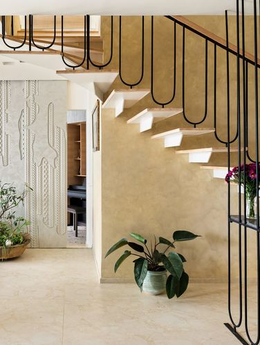 Floating wooden staircase with looped black railing against an ochre textured wall, plants below