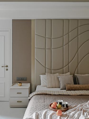 Beige tufted headboard with curved stitching behind a bed layered with cushions and a breakfast tray