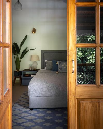 View through open wooden glass-paned door into bedroom with grey headboard and diamond rug
