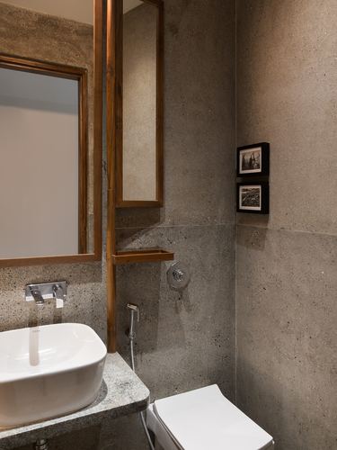 Textured stone bathroom with teak-framed mirror, vessel sink, and wall-hung toilet