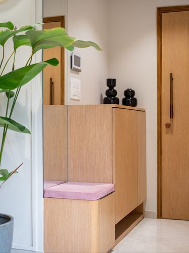 Wooden foyer cabinet with pink cushioned seat beside doors and black vases