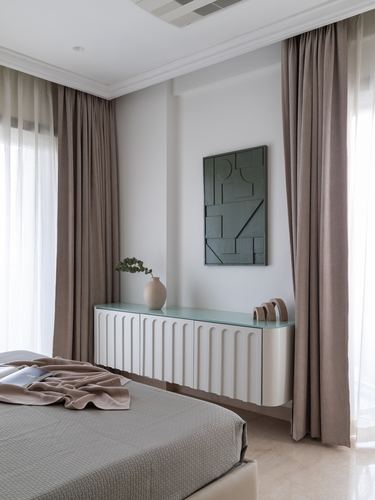 Bedroom with fluted white sideboard, dark textured wall art, and floor-to-ceiling taupe curtains