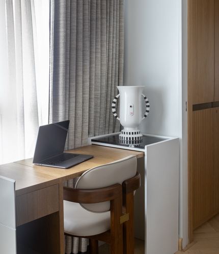 Study nook with wooden desk, laptop, pleated curtain, and striped ceramic vase on cabinet
