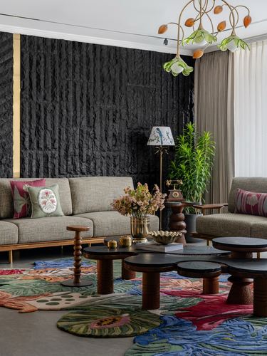 Living room with black textured feature wall, floral chandelier, and cluster of round coffee tables on colorful rug
