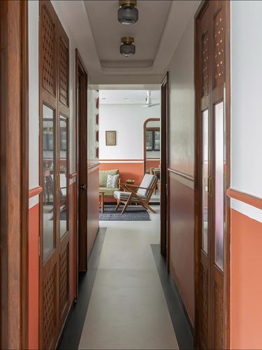 Corridor with carved wooden jaali doors opening onto a terracotta-hued living room beyond