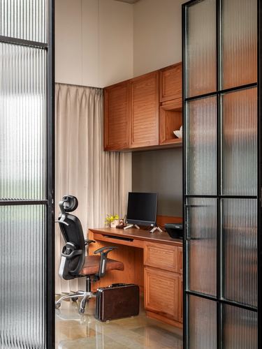 Home office nook with wooden desk, cabinetry and ergonomic chair seen through fluted glass door