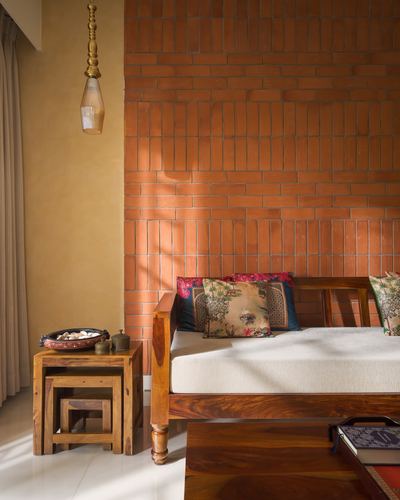 Wooden daybed with patterned cushions against a terracotta brick wall, sunlight streaming in