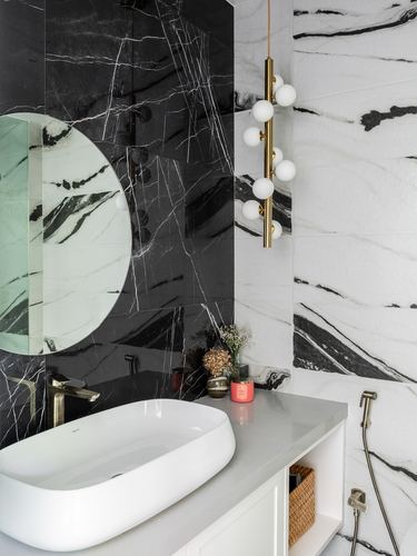 Bathroom with black and white marble walls, round mirror, brass pendant, and oval vessel sink
