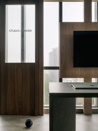 Walnut-paneled office corner with etched glass door reading Studio A-Ware, TV, and stone desk
