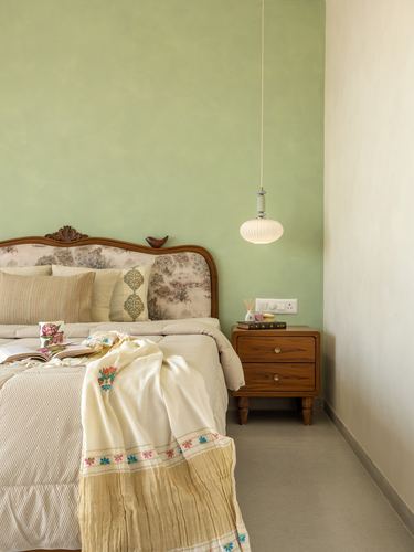 Bedroom corner with carved wood headboard, sage green wall, and hanging pendant light