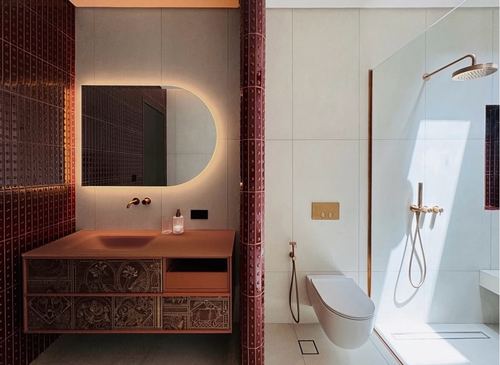 Bathroom with maroon studded tile vanity wall beside a beige tiled wet room with brass shower fixtures