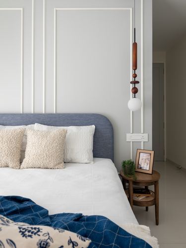 Bedroom corner with grey paneled wall, blue upholstered headboard, wooden pendant lamp and round side table