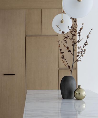 Wood-paneled kitchen corner with marble counter, black and brass vases, and globe pendant lights