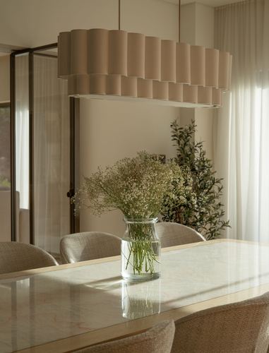 Dining table with marble-look top and glass vase of baby's breath under a large pleated pendant light