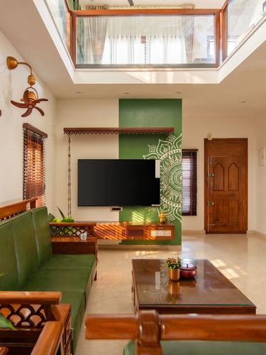 Living room with green sofa, wall-mounted TV on mandala wall, skylight above
