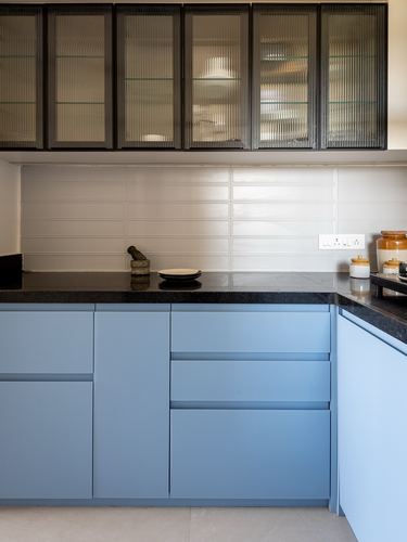 Blue kitchen cabinetry with black countertop and ribbed glass upper cabinets, white tiled backsplash