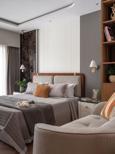 Bedroom with upholstered leather-trimmed bed, dark stone accent wall, wooden shelving and cream armchair