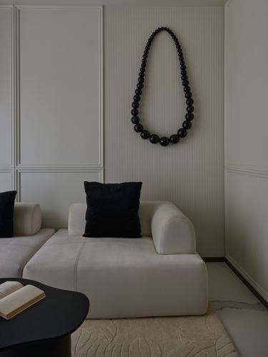 Beige modular sofa with black cushion beneath a large black bead wall sculpture on fluted panel