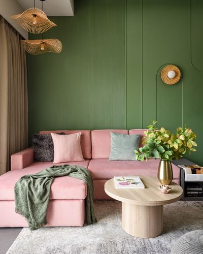 Pink velvet sectional against fluted green wall with rattan pendant lights and round wood coffee table
