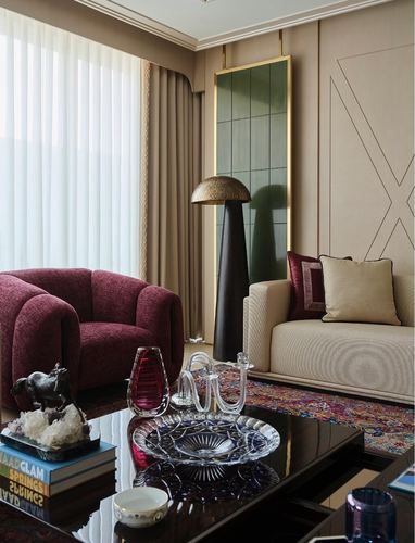 Living room corner with burgundy armchair, cream sofa, brass floor lamp and glossy coffee table with crystal objects