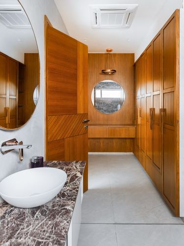Wood-paneled dressing room and bathroom with round mirrors, marble vessel sink, and stone flooring