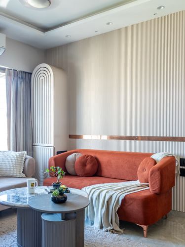 Living room with terracotta sofa against fluted beige wall and arched cabinet, round marble coffee tables in front.