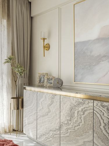 Marbled console with brass trim beneath abstract art and brass wall sconce, curtains beside