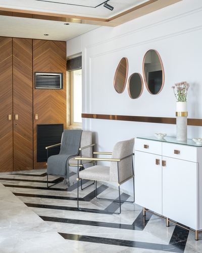 Foyer with chevron wood paneling, marble geometric floor, two armchairs, and cluster mirrors above white sideboard
