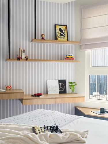 Child's bedroom corner with striped wallpaper, floating wood shelves, desk, and window seat