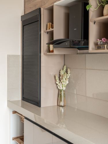 Beige kitchen counter with vase of flowers, black chimney hood, and open shelving above