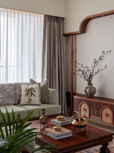 Living room corner with sage sofa, patterned cushions, brass artefacts on wooden table, and carved wood console.