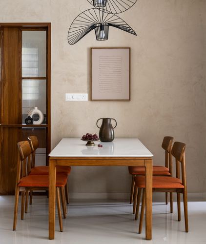 Dining table with orange chairs against a textured stucco wall and framed art