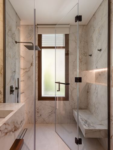 Marble bathroom with glass shower enclosure, black fixtures, frosted window, and floating marble bench