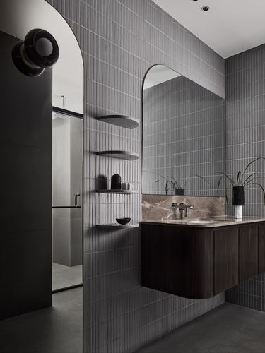 Grey ribbed-tile bathroom with arched mirror over dark wood vanity and stone countertop