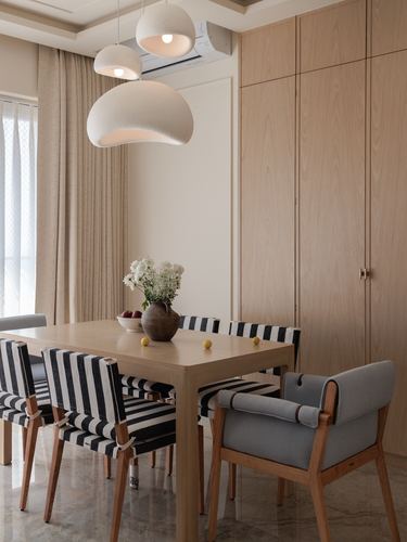 Dining table with striped chairs beneath three sculptural pendant lights, wooden cabinetry behind