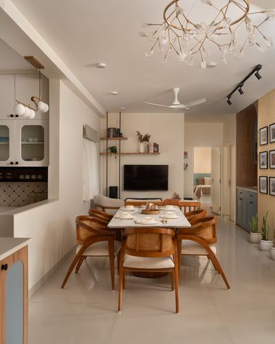 Dining room with cane-backed wooden chairs around a marble-top table under a branch chandelier
