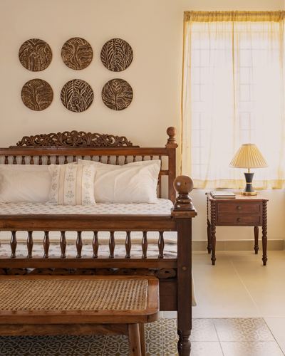 Carved wooden bed with cane bench, round carved wall panels, and sunlit window in a warm-toned bedroom