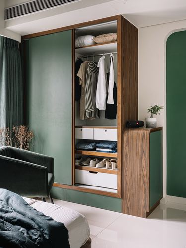 Open wardrobe with wood interior, folded clothes, shoes, and green sliding doors beside a green velvet chair