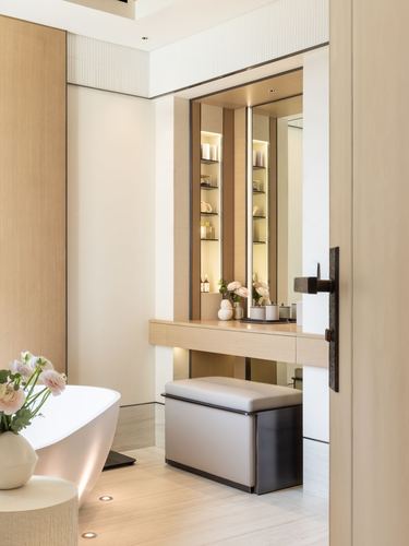 Bathroom vignette with freestanding tub, backlit vanity niche, and leather ottoman seen through open door