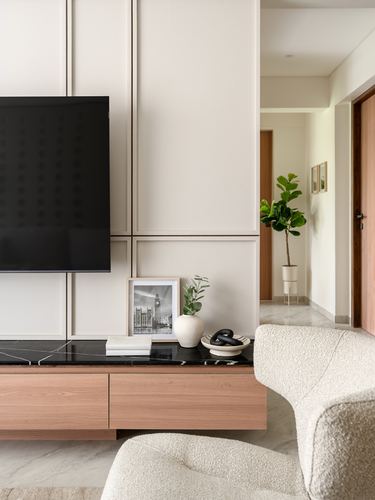 Living room console with tv, marble top, wood drawers and boucle armchair beside a hallway with a plant