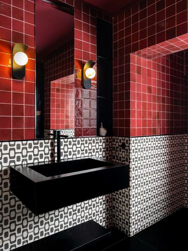 Bathroom with red tiled upper wall, black and white patterned lower wall, black floating sink and mirror