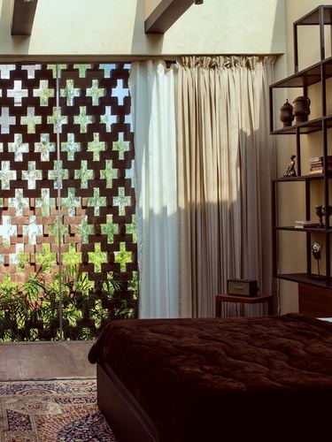 Bedroom with dark wooden jali screen window, cream curtains, and open metal shelving unit