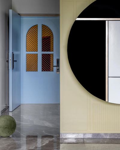 Foyer with arched blue door, striped amber glass panels, marble floor, and large black circular mirror on yellow wall