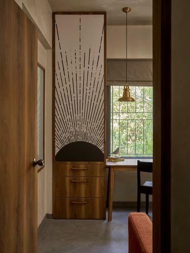 Wooden door opens to a study nook with a sunburst-patterned cabinet and window desk beyond.